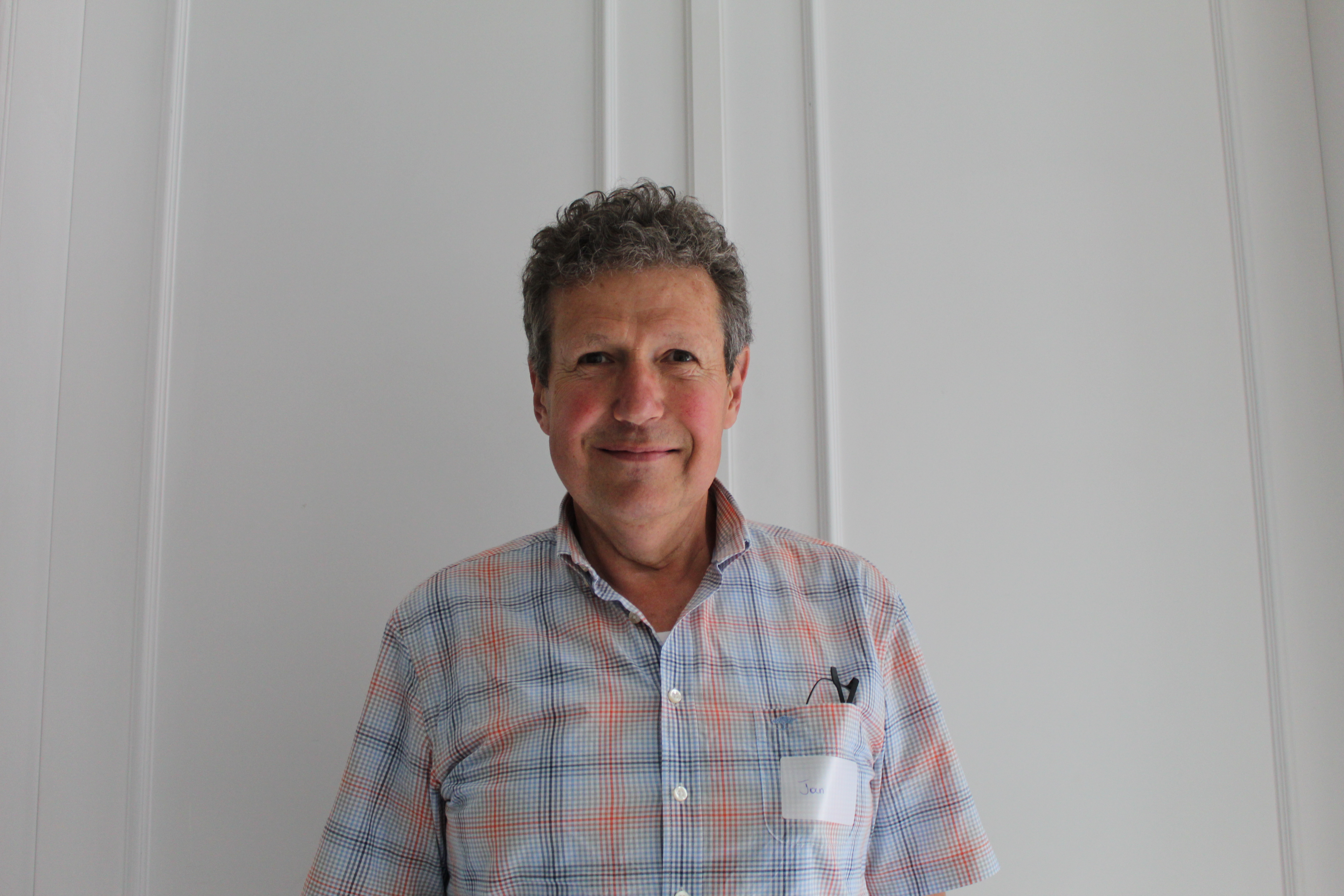 Middle aged man with short curly hair, wearing a printed button up blouse and warmly smiling to the camera